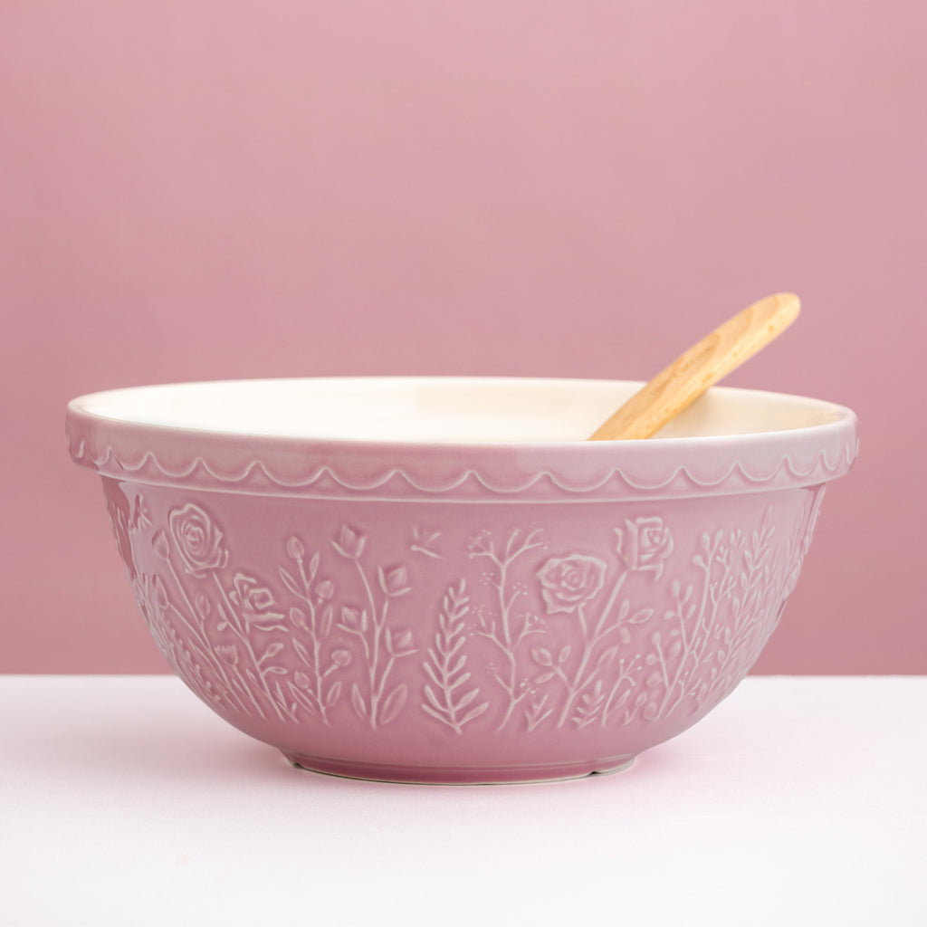 Pink ceramic bowl with floral patterns and a wooden spoon on a pink background