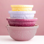 Stack of embossed ceramic bowls in pastel colors on a pink background