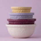 Stack of embossed ceramic bowls in various colors on a light purple background