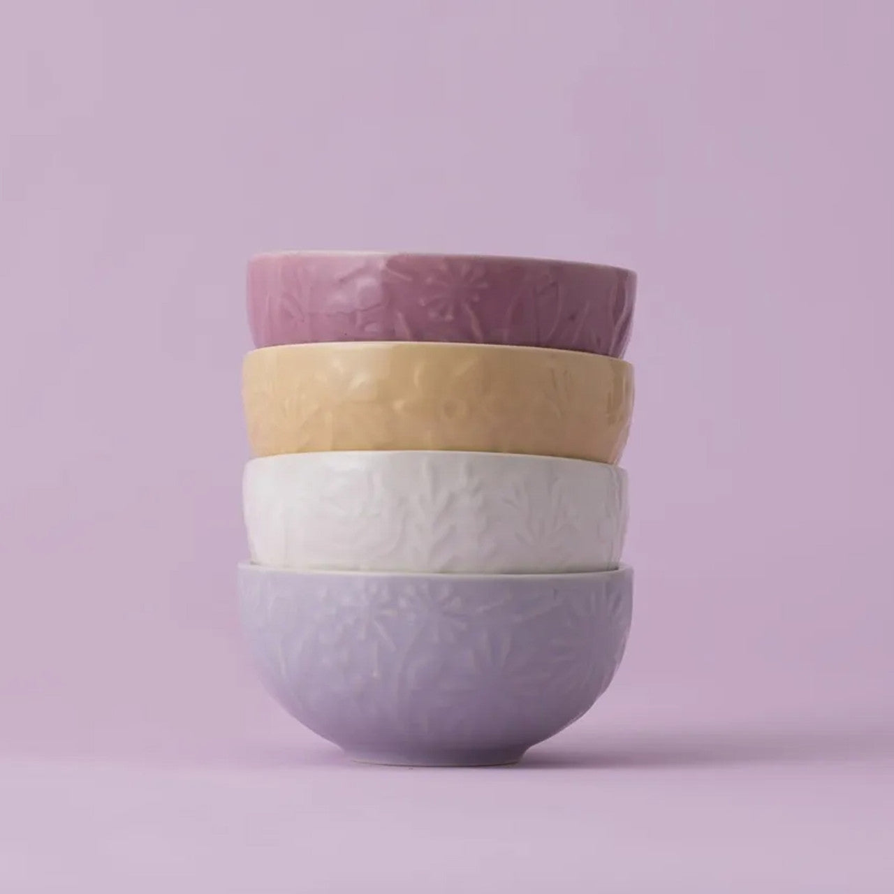 Stack of four ceramic bowls with floral patterns on a light purple background