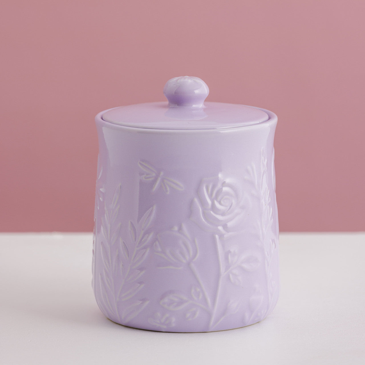 Lavender ceramic jar with floral embossing on a pink background
