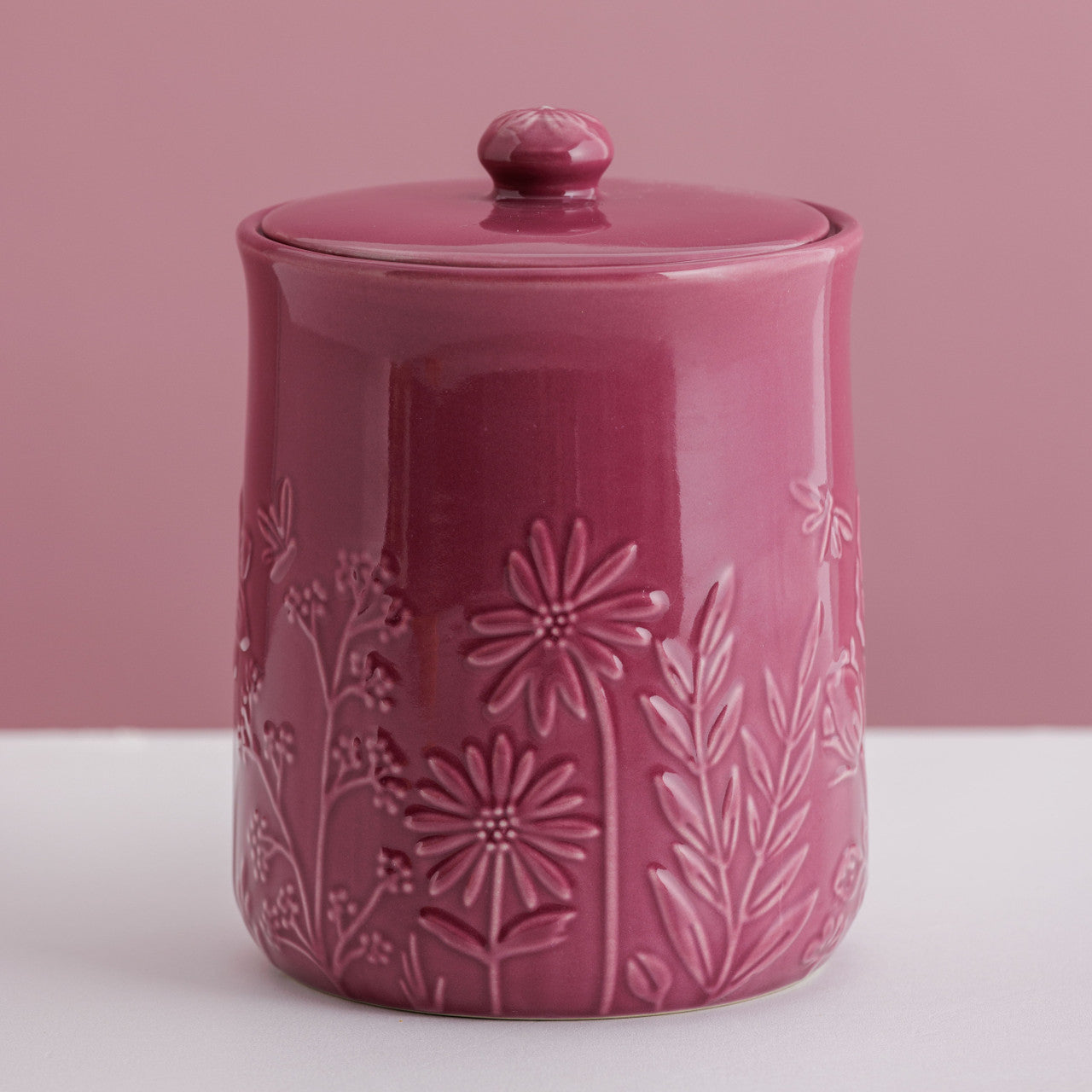 Pink ceramic jar with floral embossing on a pink background