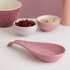 Pink ceramic spoon and bowls with a floral pattern on a white surface.