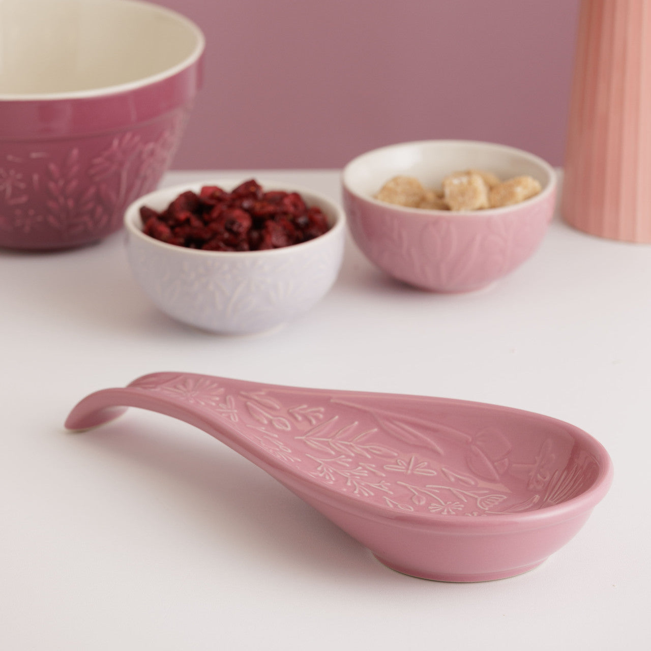Pink ceramic spoon and bowls with a floral pattern on a white surface.