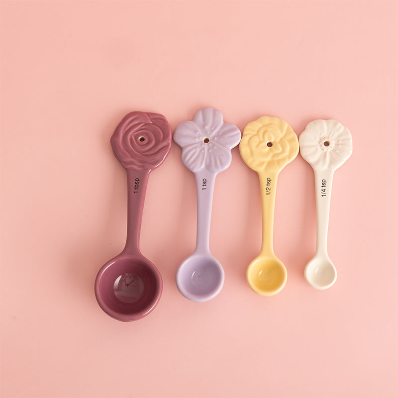 Four floral-themed measuring spoons in different colors on a pink background